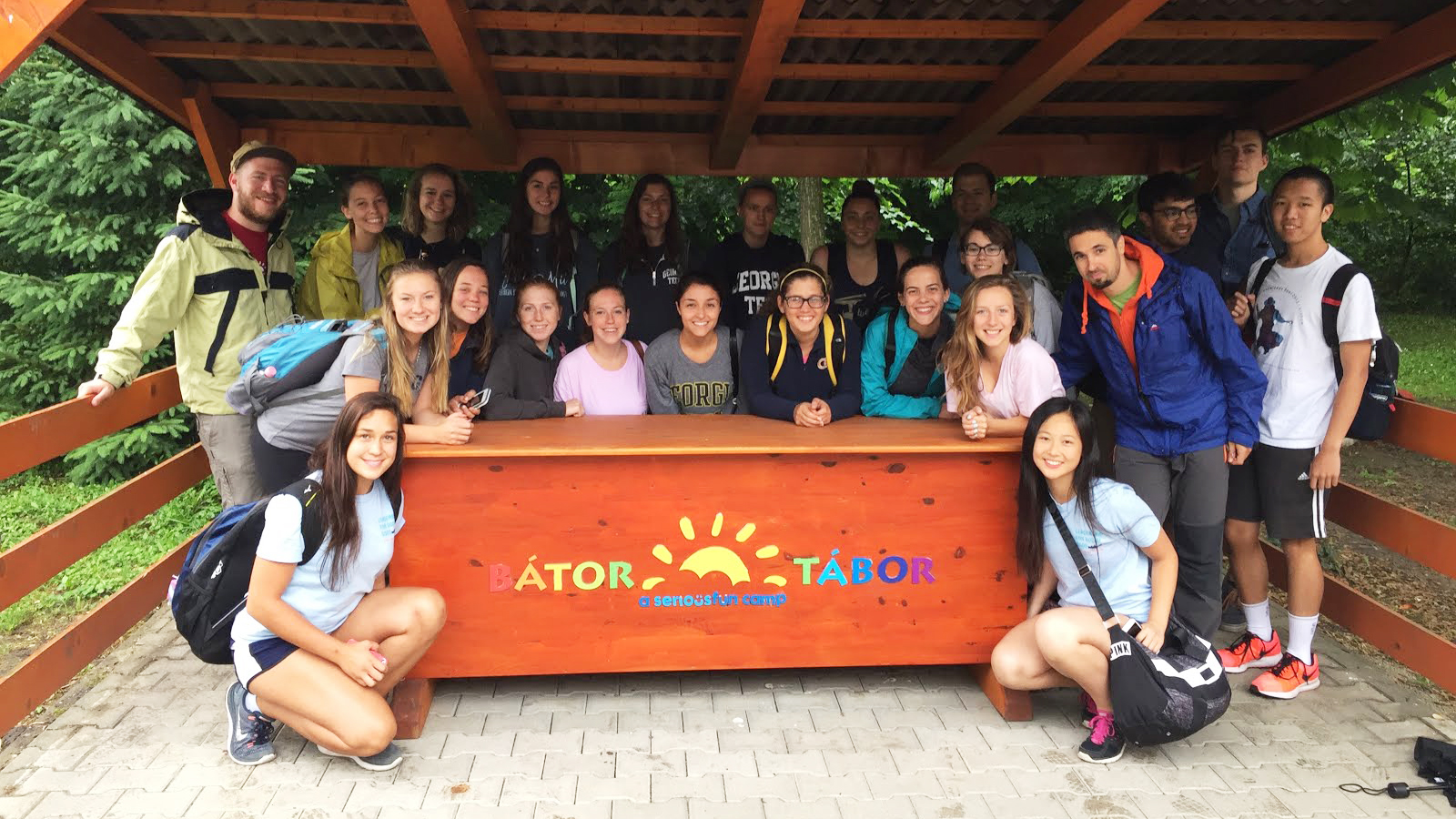 Group photo of Tech students standing under a metal awning and gathered around a counter that has Bator Tabor, a serious fun camp emblazoned on it 