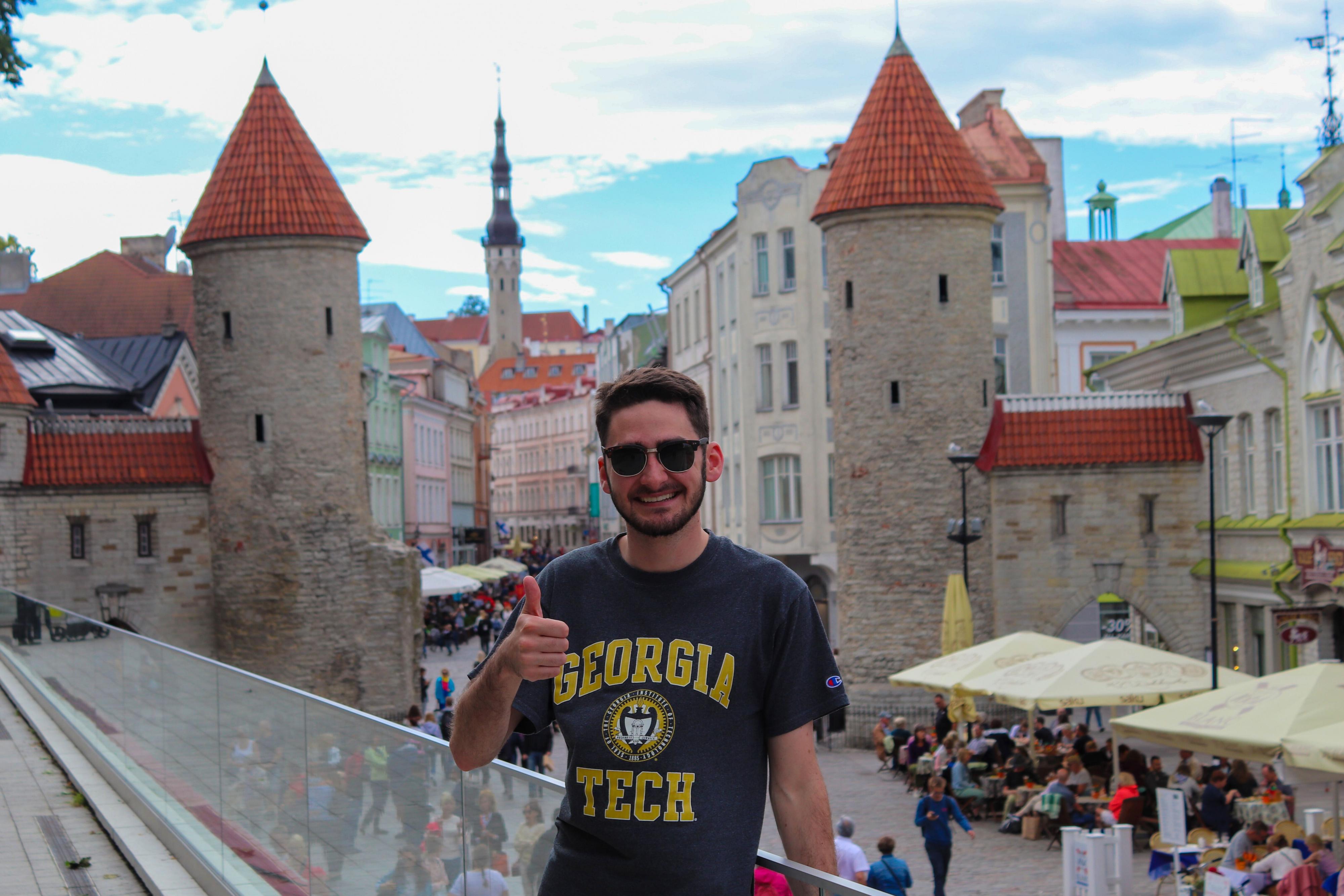 Student wearing a Georgia Tech tshirt giving a thumbs up while standing on a balcony overlooking a city in Latvia