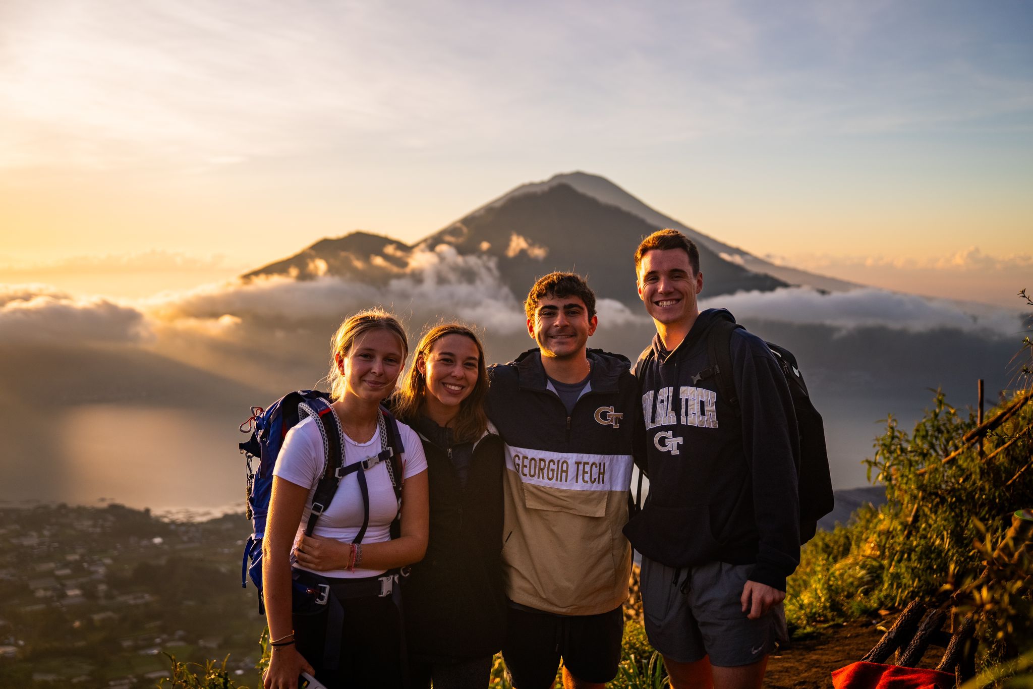 A group of four GA Tech students stands with a body of water and mountains in the background